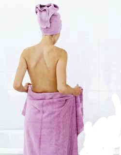 Young woman taking off a towel standing by a bathtub